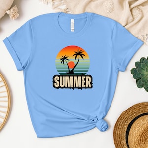 Peut inclure: Un t-shirt bleu clair avec un graphique de coucher de soleil r&eacute;tro repr&eacute;sentant des palmiers et le mot "SUMMER" dans une police d'&eacute;criture us&eacute;e.