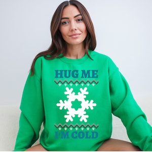 May include: Green sweatshirt with a white snowflake and the text "HUG ME I'M COLD" in blue.