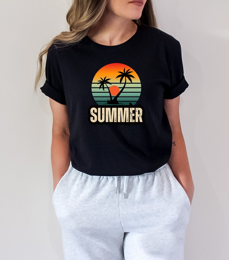 Peut inclure: Un t-shirt noir avec un motif r&eacute;tro de palmiers et un coucher de soleil. Le motif est dans des tons d'orange, jaune et bleu. Le texte "SUMMER" est imprim&eacute; sous le motif.