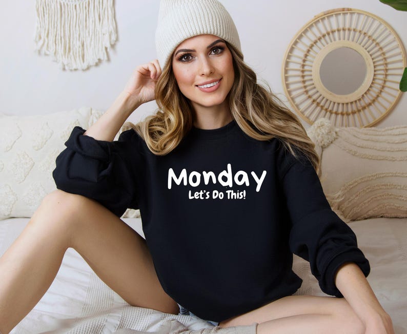 May include: Black sweatshirt with white text that reads "Monday Let's Do This!" A woman is wearing the sweatshirt and a white beanie.