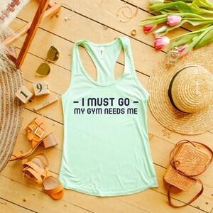 Puede incluir: Un top de tirantes verde claro con el texto "I must go - my gym needs me" en letras azul marino.