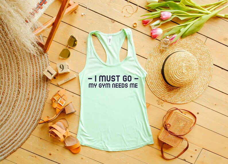 Puede incluir: Un top de tirantes verde claro con el texto "I must go - my gym needs me" en letras azul marino.