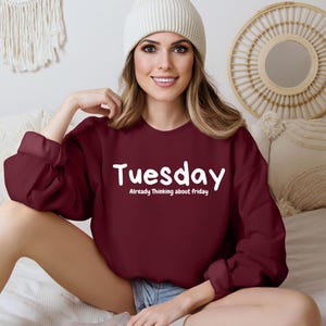 May include: A maroon sweatshirt with the text "Tuesday" and "Already Thinking about Friday" in white lettering.