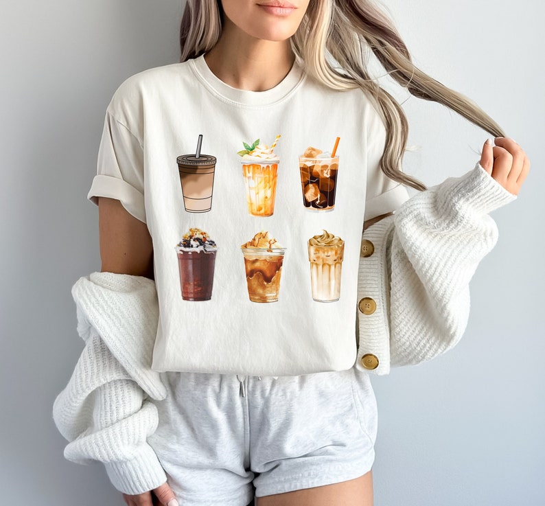 May include: A white t-shirt with a graphic of six different iced coffee drinks. The drinks are all in clear cups with different toppings and flavors.