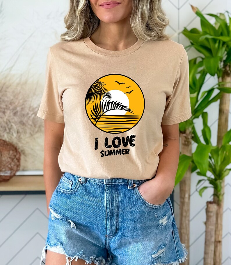 May include: A beige t-shirt featuring a graphic of a palm tree, sun, and birds within a yellow circle. The text "i love summer" is printed beneath the circle.