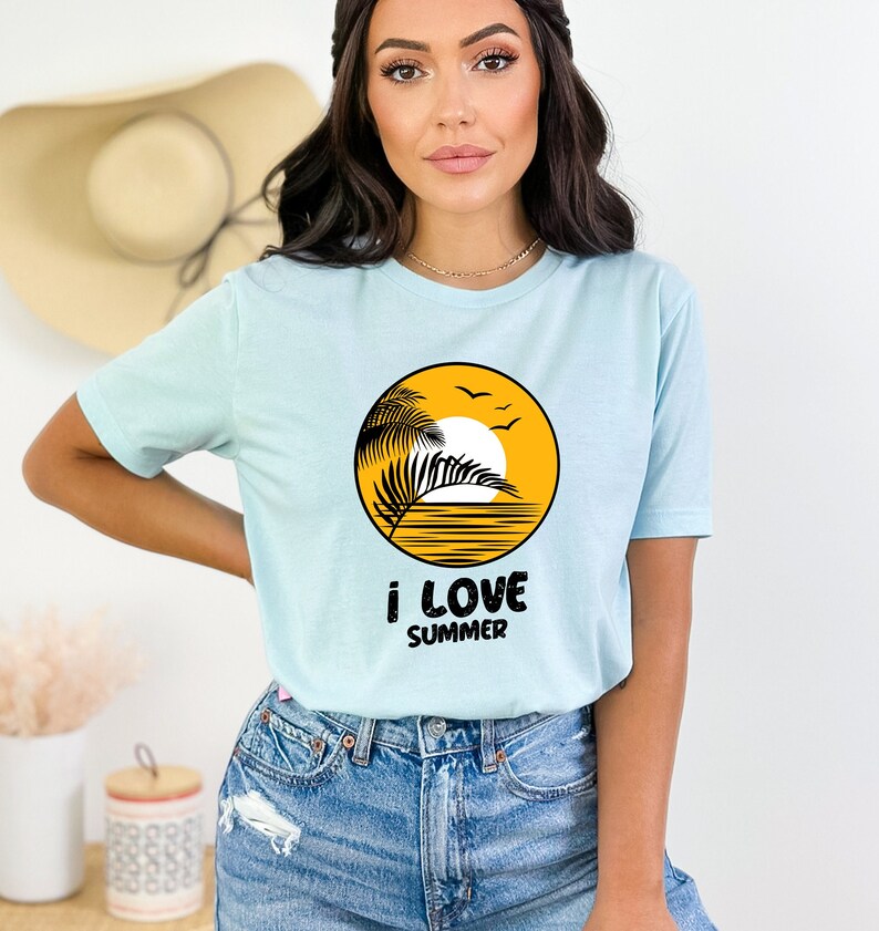 May include: A light blue t-shirt with a yellow circle graphic of a palm tree, sun, and ocean waves. The text "i love summer" is printed below the graphic.