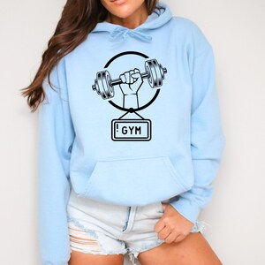 May include: Light blue hooded sweatshirt with a black graphic of a hand lifting a dumbbell with a sign that says "!GYM".