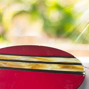 May include: A round, red glass serving tray with three gold and black stripes.