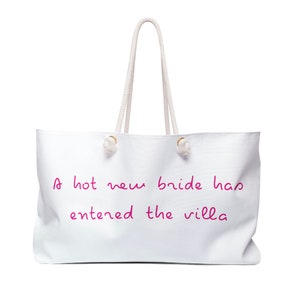 May include: White canvas tote bag with white rope handles and a pink inscription that reads "A hot new bride has entered the villa".