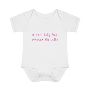 May include: White babygrow with pink text that reads "A new baby has entered the villa".