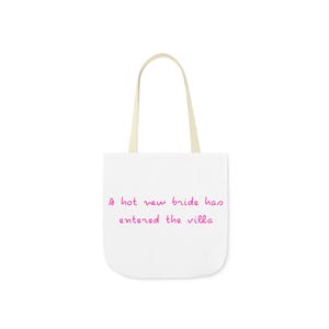May include: White tote bag with cream-colored handles. The bag features the text "A hot new bride has entered the villa" in pink script. The bag is designed for carrying items.