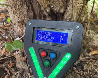 May include: A black electronic scoreboard device with a blue LCD screen displaying text: DOMINATION 17:51, RED SCORE: 0, GREEN SCORE: 64, BLUE SCORE: 0. The unit features three circular buttons in red, blue, and green, and two vertical green light strips.