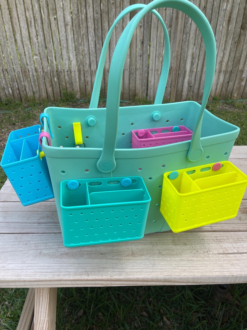 May include: A large, teal tote bag with matching teal handles and several colourful, removable organiser inserts. The inserts are blue, pink, and yellow. The bag and inserts are made of a durable, perforated material.