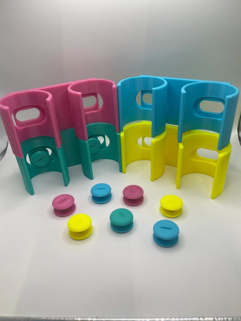 May include: A set of colorful plastic toy building blocks in pink, teal, yellow, and blue. The blocks have a curved design with a handle-like opening at the top. Several small, round, two-toned pieces in matching colors are also included.