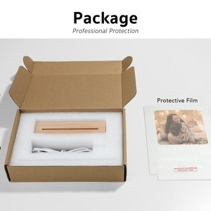 Puede incluir: Una caja de cart&oacute;n marr&oacute;n con un interior de espuma blanca. La caja contiene una base de madera, un cable blanco y una pel&iacute;cula protectora. La pel&iacute;cula protectora es transparente y tiene una imagen de una familia. El texto en la pel&iacute;cula protectora dice "Retire el envoltorio antes de usar".