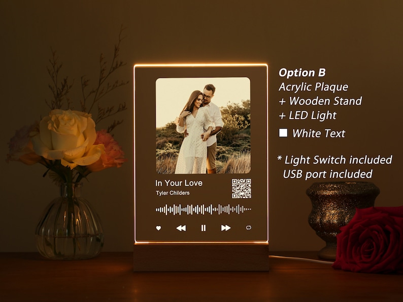 Puede incluir: Una placa de acr&iacute;lico personalizada con una foto de una pareja, un t&iacute;tulo de canci&oacute;n y el nombre del artista, "In Your Love" de Tyler Childers, y un c&oacute;digo QR. La placa tiene un soporte de madera y una luz LED blanca. El texto es blanco.