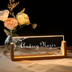 May include: A wooden desk sign with a clear acrylic insert. The insert has a decorative design and the text "Andrey Mazir, General Manager" in white lettering.