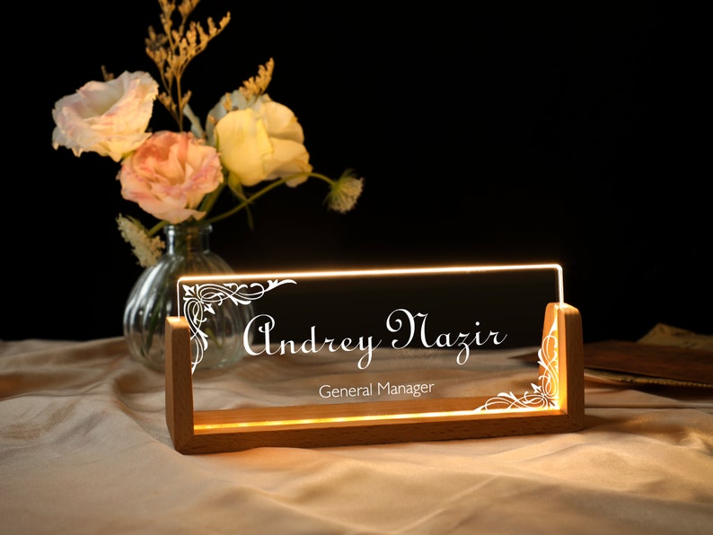 May include: A wooden desk sign with a clear acrylic insert. The insert has a decorative design and the text "Andrey Mazir, General Manager" in white lettering.