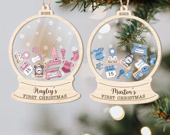 May include: Two wooden snow globe ornaments with personalized details. One features pink accents and the name "Hayley's First Christmas," while the other has blue accents and "Marton's First Christmas." Both include the year 2025 and snowflake designs.
