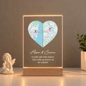 Op de afbeelding: Een rechthoekige acrylplaat met een hartvormige kaartafbeelding die Sydney en Wenen toont, verbonden door een stippellijn. De plaat bevat de namen Mason & Sienna en de tekst CLOSE OR FAR AWAY, YOU ARE ALWAYS IN MY HEART, op een houten voet.