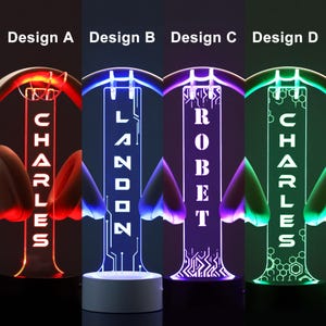 Puede incluir: Cuatro luces nocturnas LED iluminadas con nombres personalizados. Cada dise&ntilde;o presenta un color diferente: rojo, azul, morado y verde. Los nombres "Charles", "Landon", "Robert" y "Charles" se muestran verticalmente. Las bases son blancas o negras.