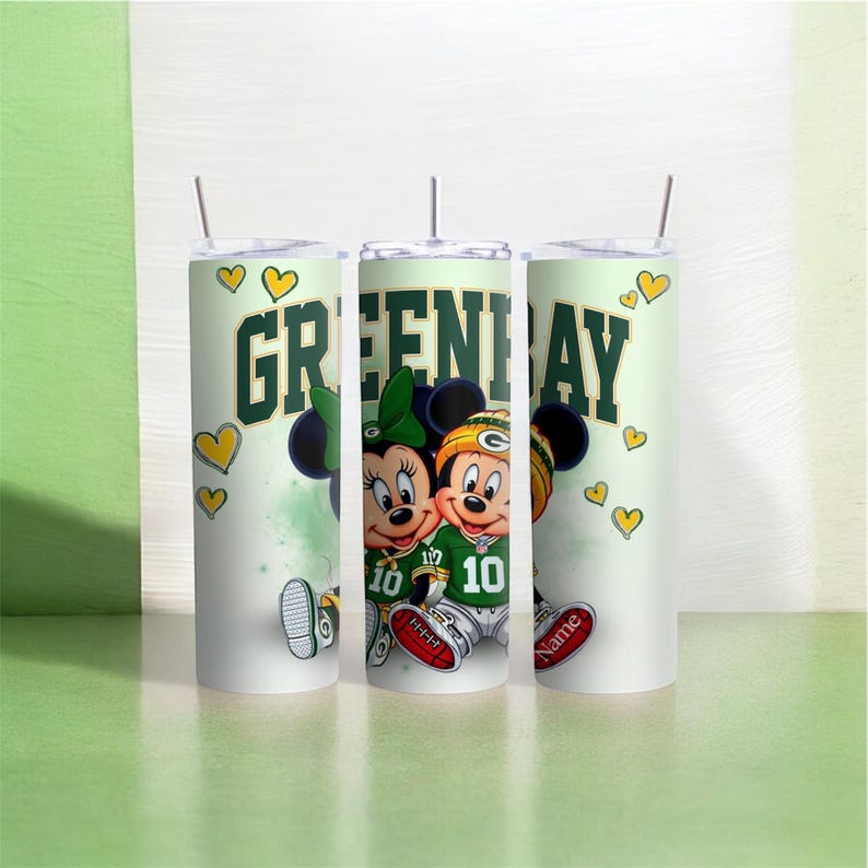 K&ouml;nnte beinhalten: Ein wei&szlig;er Becher mit einem gr&uuml;n-gelben Design mit Mickey und Minnie Mouse in Football-Kleidung. Der Becher hat die Worte "GREEN BAY" in Gr&uuml;n und Gelb, mit gelben Herzakzenten. Die Nummer 10 steht auf den Trikots.