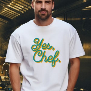May include: White t-shirt with a teal and yellow graphic that says "Yes, Chef."