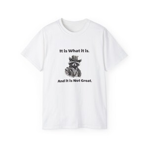 May include: White t-shirt with a black and white illustration of a raccoon wearing a hat and the text "It is What it is. And it is Not Great."