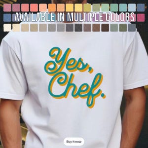 Peut inclure: Un t-shirt blanc à manches courtes avec le texte Yes, Chef. écrit dans une police sarcelle stylisée avec une ombre portée dorée. Au-dessus du texte, une grille de petits carrés colorés affiche le texte blanc AVAILABLE IN MULTIPLE COLORS.