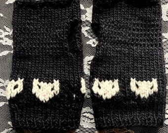 May include: A pair of black knitted fingerless gloves with white cat faces embroidered on each glove.