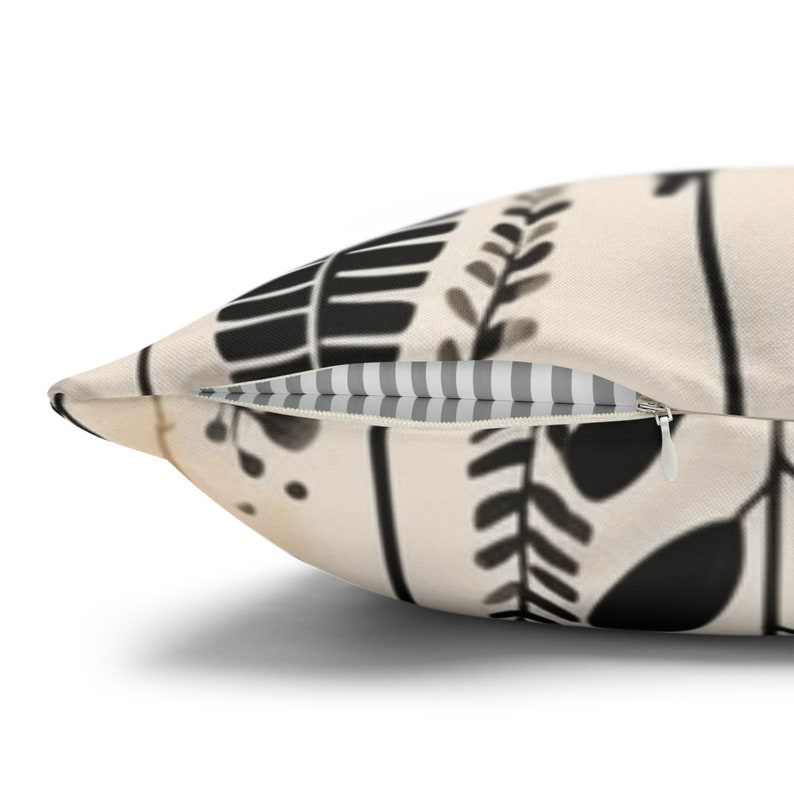 May include: A cream-colored pillow with a black and white floral pattern. The pillow has a zipper closure and a gray and white striped lining.