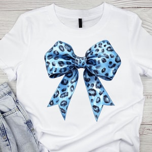 May include: A white t-shirt with a blue and black leopard print bow on the front.