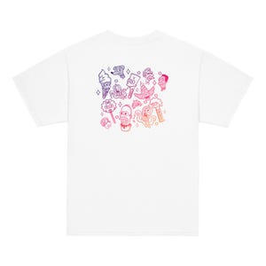 Pode incluir: Camiseta branca com um gráfico colorido de personagens de desenhos animados. O design inclui casquinhas de sorvete, um cachorro e outras ilustrações caprichosas em tons de rosa, roxo e laranja.