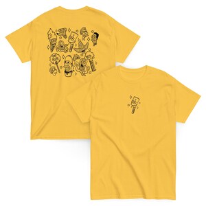 Pode incluir: Duas camisetas amarelas. Uma camiseta apresenta um desenho de desenho animado em preto e branco nas costas, com vários personagens. A outra camiseta tem um único personagem de desenho animado na frente. Ambas são de manga curta.