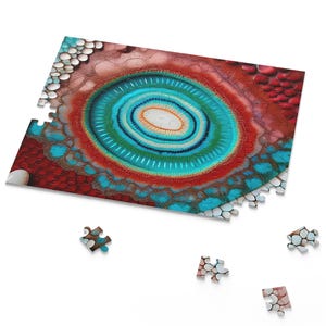 Könnte beinhalten: Ein teilweise zusammengesetztes Puzzle mit einem abstrakten Design aus konzentrischen Kreisen in Blau, Grün, Rot und Weiß. Mehrere Puzzleteile sind um das Hauptpuzzle herum verstreut, vor einem weißen Hintergrund.