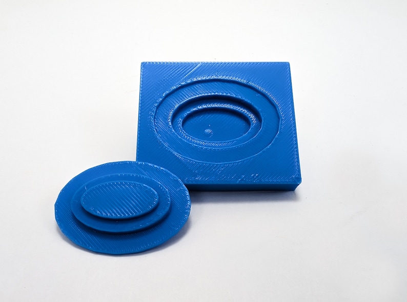 Pu&ograve; includere: Uno stampo in plastica blu stampato in 3D per la creazione di gioielli in resina. Lo stampo &egrave; in due pezzi, una base quadrata e un top ovale separato. Lo stampo ha tre forme ovali concentriche.