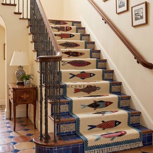 May include: Staircase with beige carpet runners featuring colorful fish designs. The runners are bordered with blue trim and fringe, complementing the blue tile risers. A wooden handrail and decorative newel post are visible.