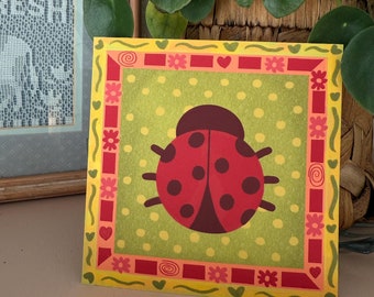 May include: A yellow square card with a red ladybug on a green background. The ladybug has black spots and a red body. The card has a red and yellow border with flowers and hearts.