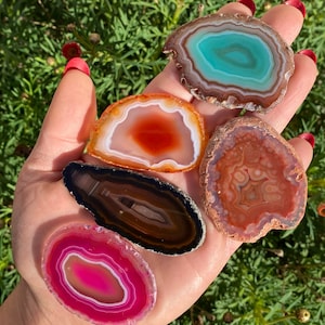 May include: A selection of polished agate slices in shades of teal, orange, brown, and pink. Each slice features distinctive banding patterns and natural textures, highlighting the beauty of the gemstones. These decorative stones are suitable for home decor or crafting projects.