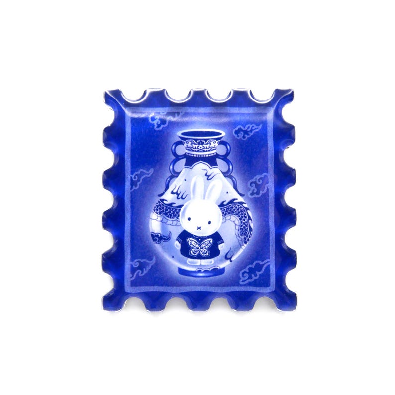 Pu&ograve; includere: Un francobollo decorativo blu con un personaggio di coniglio bianco che indossa una camicia blu con un disegno a farfalla. Il coniglio &egrave; ambientato contro un vaso blu con un disegno di drago. Il francobollo ha un bordo smerlato e uno sfondo bianco.