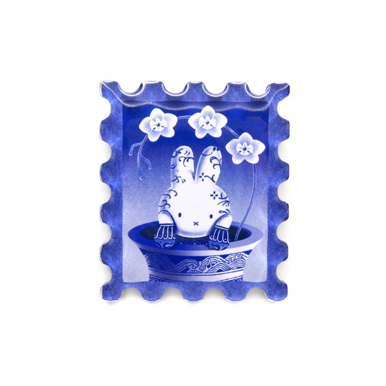Pu&ograve; includere: Illustrazione blu e bianca di un coniglietto in un vaso decorativo, incorniciata da un bordo di francobollo blu. Il coniglietto ha un design floreale ed &egrave; circondato da fiori bianchi. L'opera d'arte ha un'estetica vintage in porcellana.