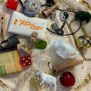 May include: A collection of miscellaneous small objects including a white Travelodge matchbox, a red die, a miniature white sheep figurine, a ceramic owl, a brass hook, a metal padlock, a shell, a glass teapot, a cherry, and a yin-yang charm.