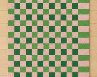 May include: A rectangular rug with a checkerboard pattern in green and pink. The rug has a green border with a wavy pink line. The checkerboard pattern is made up of alternating green and pink squares.