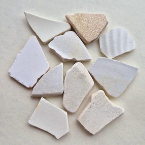 May include: A collection of ten white ceramic tile pieces, some with a textured surface, arranged in a circular pattern on a light beige background.