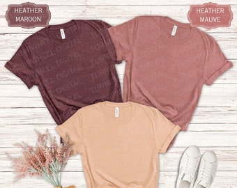May include: Three blank t-shirts in different colors: heather maroon, heather mauve, and heather peach. The shirts are laid out on a white wooden surface.