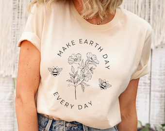 May include: A soft cream t-shirt featuring a black line art graphic of a central flower bouquet flanked by two bees. The text "MAKE EARTH DAY" is arched above the flowers, and "EVERY DAY" is arched below in a simple, clean sans-serif font.