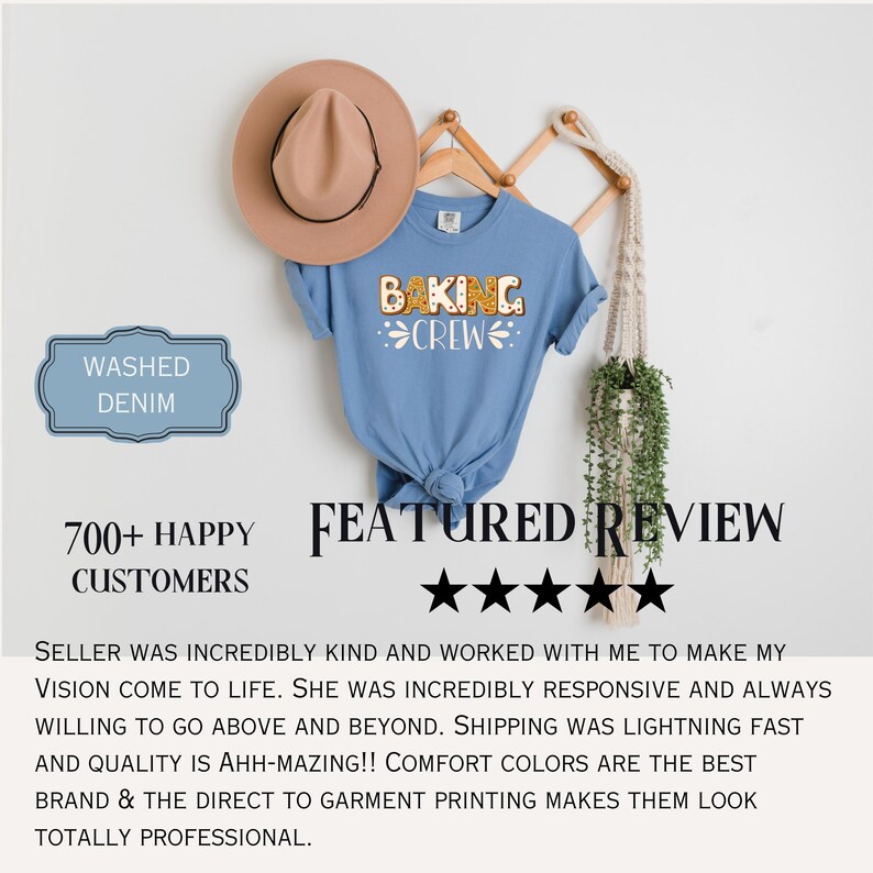 May include: A washed denim blue short-sleeve t-shirt featuring the text BAKING CREW in a gingerbread-style font with white icing details. The shirt is displayed on a wooden hanger alongside a tan fedora hat and a hanging macrame plant holder.