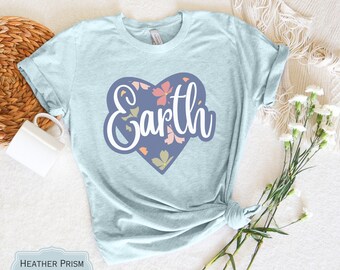 May include: A heather prism ice blue short-sleeve t-shirt featuring a central graphic of a purple heart shape filled with small pink and yellow floral accents. The word Earth is printed in large white cursive script across the heart graphic.