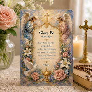 Op de afbeelding: Een religieuze kunstdruk met de tekst "Glory Be (Doxology)" omringd door engelen, bloemen en een duif. Het kunstwerk heeft een vintage stijl met zachte kleuren en een kruis bovenaan. Een kaars en rozenkrans kralen zijn op de achtergrond.