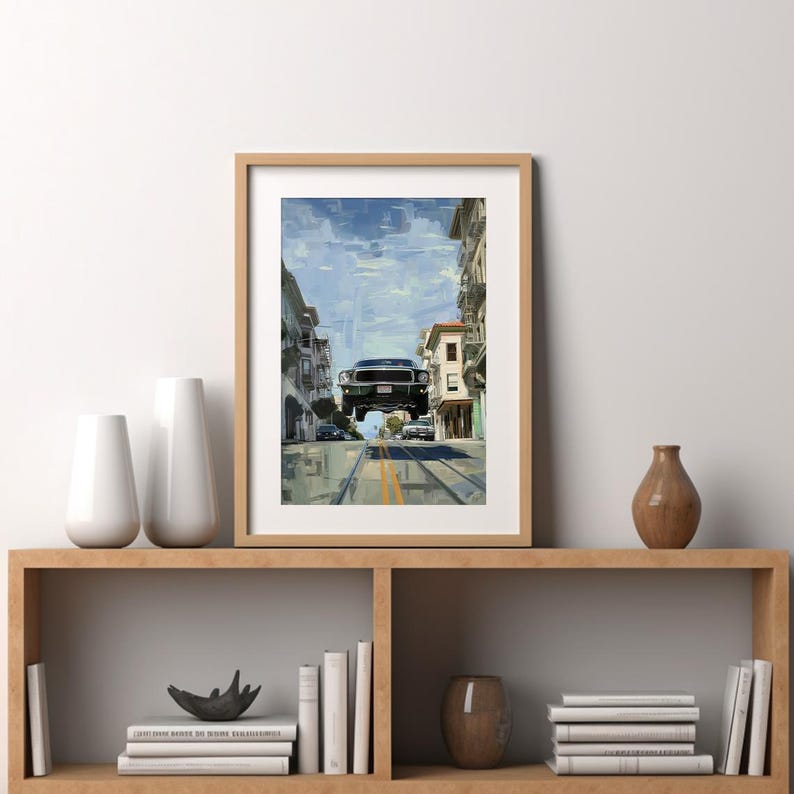Op de afbeelding: Een ingelijst afdruk van een zwarte auto die over een stadsstraat vliegt. De auto hangt in de lucht, met de voorwielen van de grond. De straat wordt aan beide kanten begrensd door gebouwen, en er zijn bomen en andere auto's op de achtergrond.